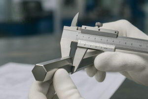 A quality control expert wearing gloves uses a caliper to precisely measure the across-flats dimension of a bright-finished stainless steel hexagon bar, A procurement manager buying stainless steel hexagon bars for a project.